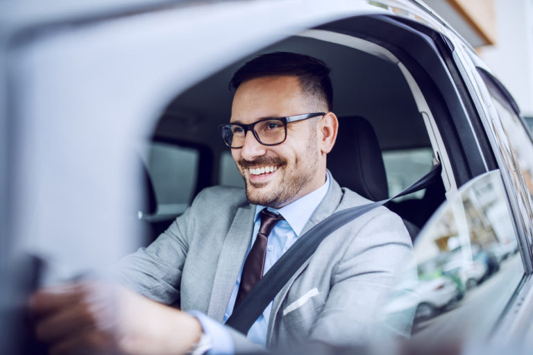 Attractive caucasian smiling elegant unshaven businessman in suit and eyeglasses driving his expensive car